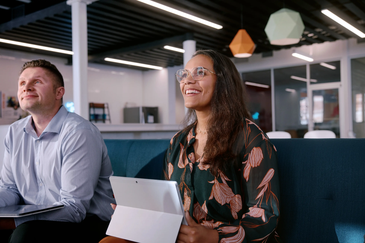 Une femme souriante assise derrière un comptoir avec un ordinateur portable ouvert devant elle.